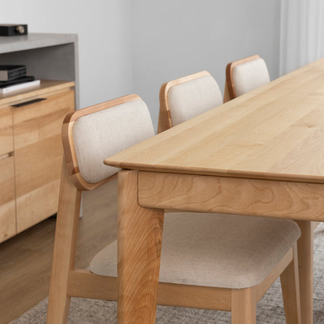 Table a manger en bois clair avec trois chaises beiges dans une salle au style minimaliste.