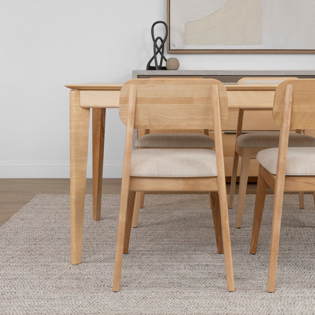 Table en bois clair avec chaises assorties en tissu beige sur tapis texture clair.