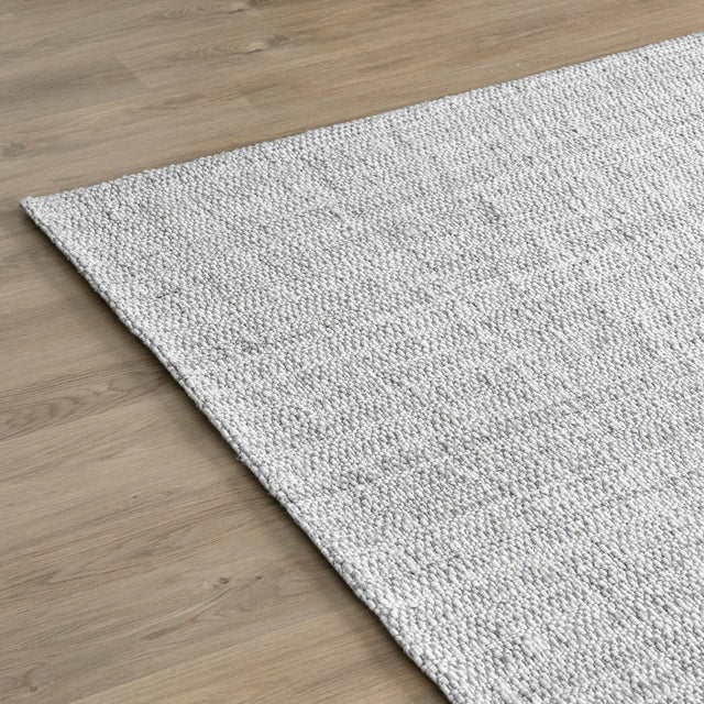 tapis gris clair texture tisse sur sol en bois clair.