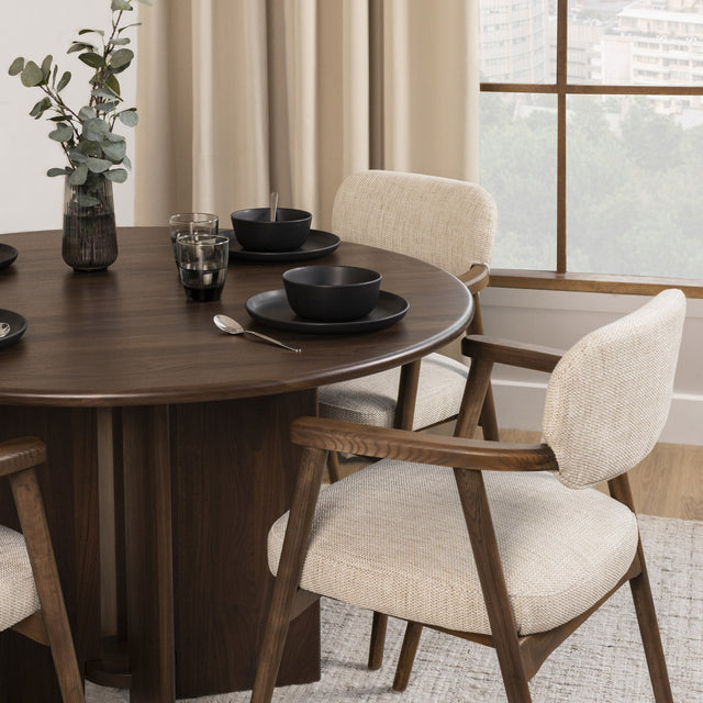 Table à manger ronde en bois foncé avec fauteuils bouclés beige style scandinave.