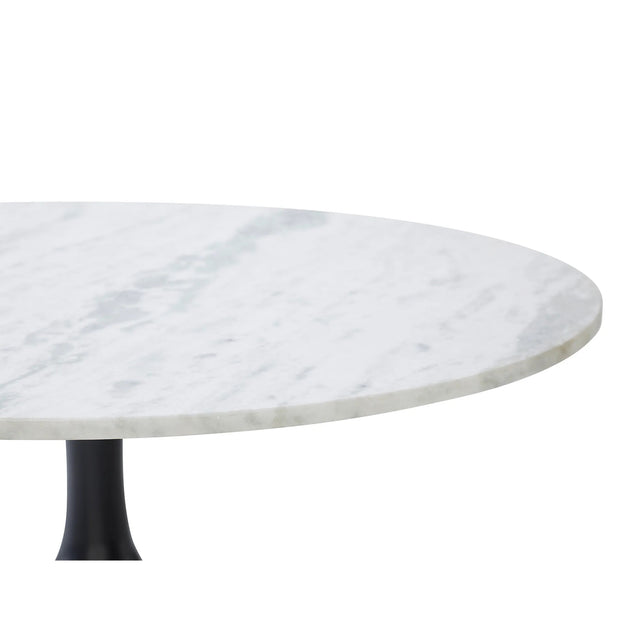 Gros plan sur le plateau rond en marbre blanc veiné d’une table au pied central noir élancé.