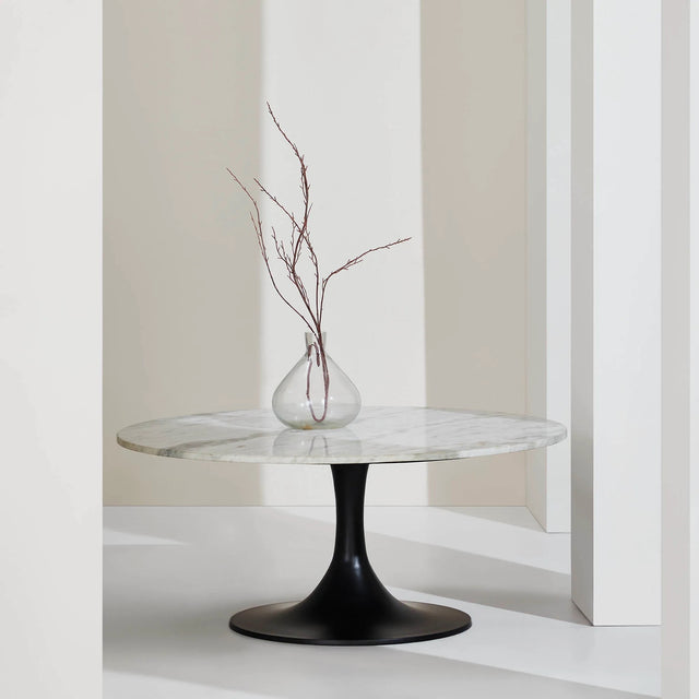 Table basse ronde élégante avec plateau en marbre blanc veiné et pied central noir tulipe, présentée dans un décor minimaliste avec un vase en verre transparent.