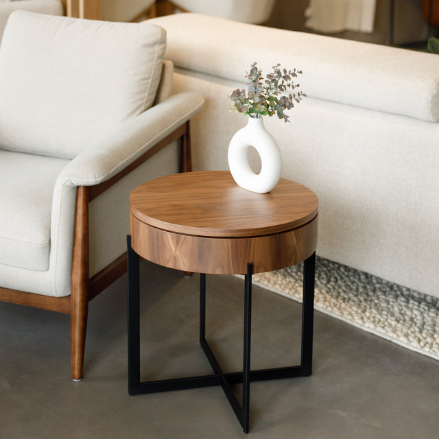 Table d’appoint ronde en bois noyer avec rangement, près d’un fauteuil beige.