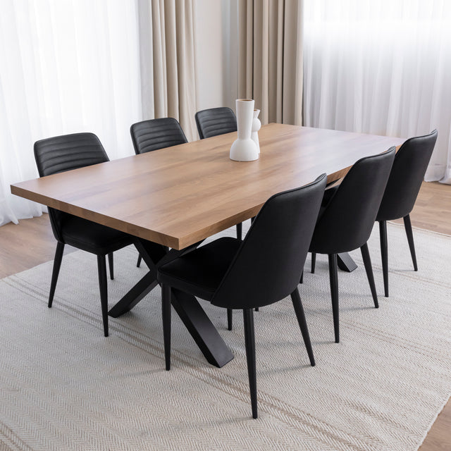 Table à manger en bois clair avec piètement en X métallique noir, entourée de six chaises noires dans une salle à manger moderne et épurée.