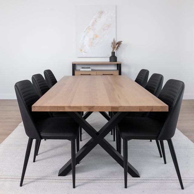 Table à manger en bois clair avec piètement en X métallique noir, entourée de six chaises noires dans une salle à manger moderne et épurée.
