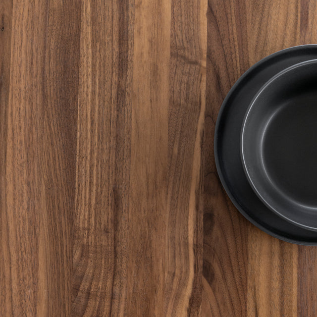 Surface de table en bois noyer avec assiette noire au design minimaliste.