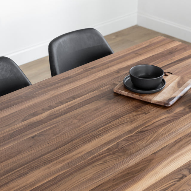 Table en bois noyer avec chaises noires et vaisselle sombre sur planche decorative.