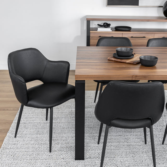 Salle a manger elegante avec table en bois, chaises noires modernes et vaisselle noire sur tapis clair.