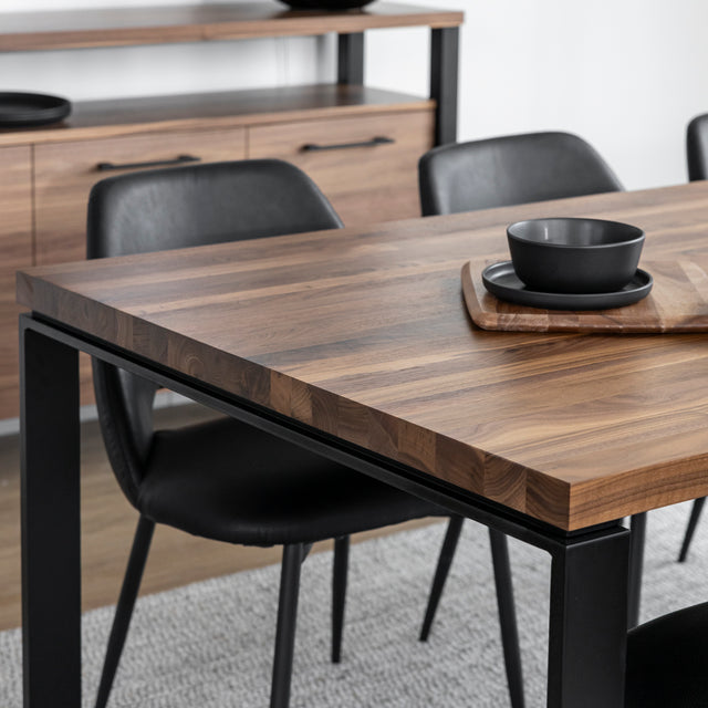 Table en bois noyer avec chaises noires et vaisselle sombre sur planche decorative.