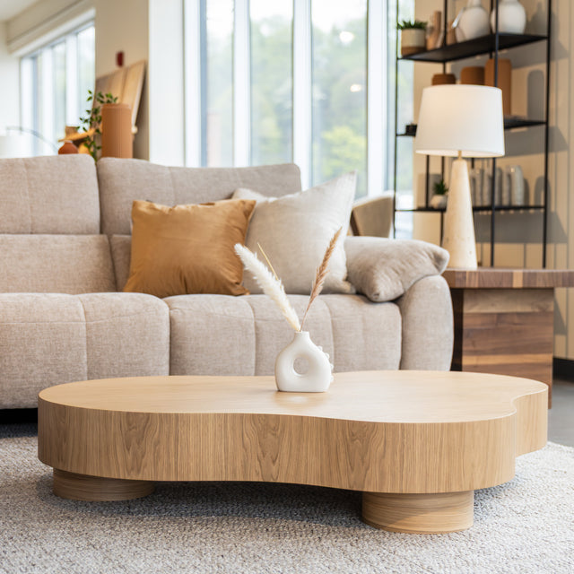 Table basse organique en bois clair dans un salon moderne avec un sectionnel gris.
