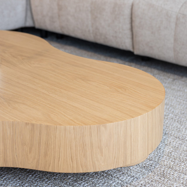 Table basse organique en bois clair dans un salon moderne avec un sectionnel gris.