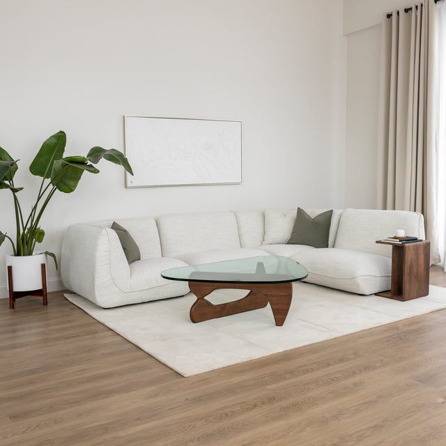 Salon moderne avec canape d angle beige et table basse en verre et bois courbe.