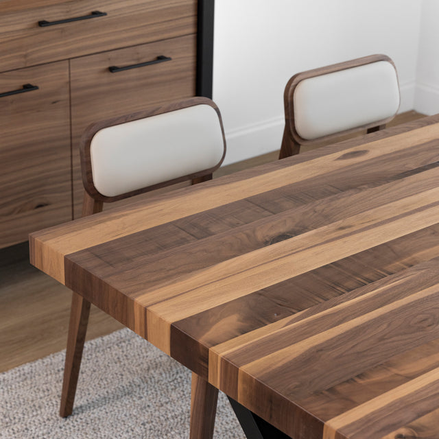 Table en bois a bandes contrastees avec chaises beige et meuble assorti en fond.
