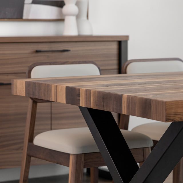 Table en bois avec pieds en metal noir et chaises beige devant buffet assorti.