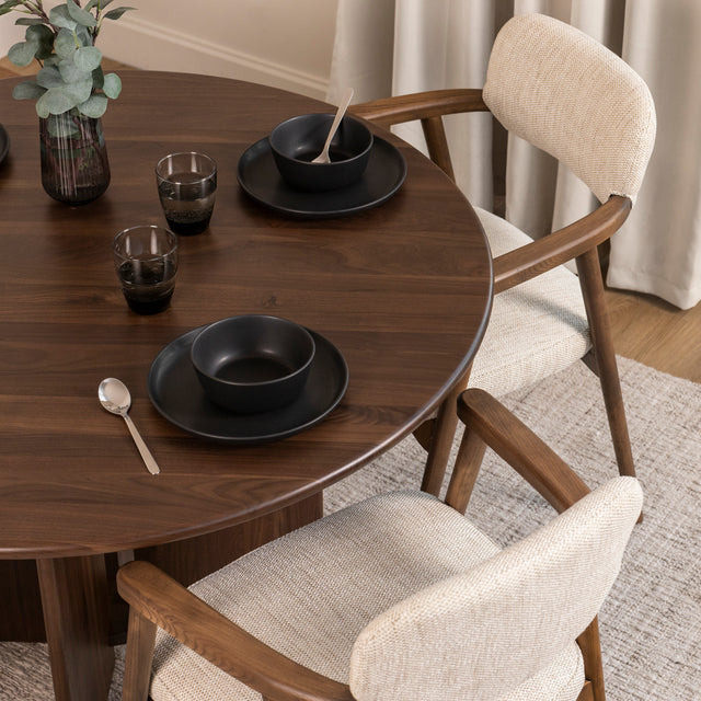 Table à manger ronde en bois foncé avec fauteuils bouclés beige style scandinave.
