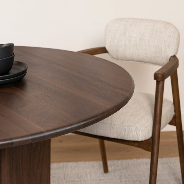 bord de table ronde en bois fonce avec chaise beige et accoudoirs bois.
