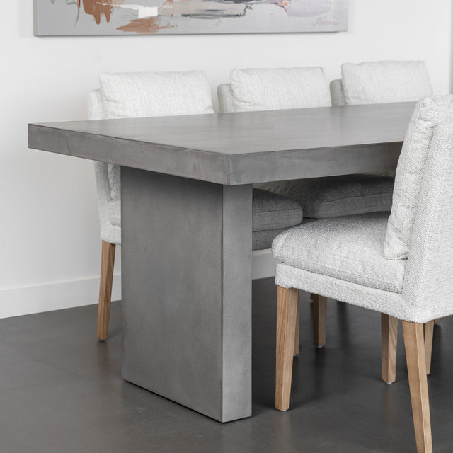 table en beton gris avec pied central massif et chaises blanches modernes.