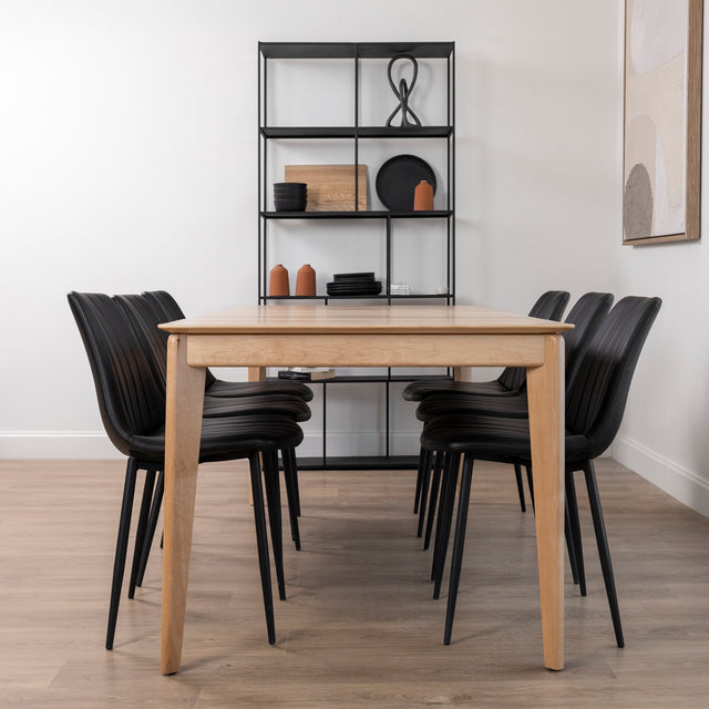 table rectangulaire en bois clair avec six chaises noires et étagère métallique en arrière-plan.