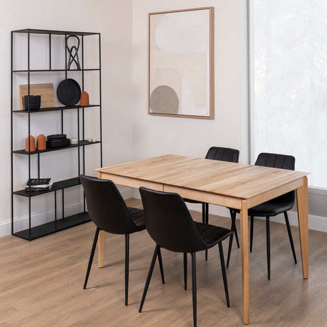 Table a manger en bois clair avec quatre chaises noires dans une salle moderne et lumineuse.