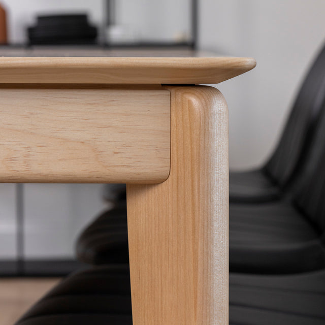 Coin de table en bois clair au design moderne, avec chaises noires en arriere-plan.