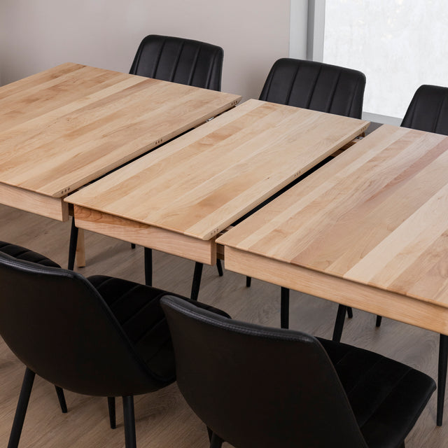 table en bois clair extensible avec rallonges centrales et chaises noires.