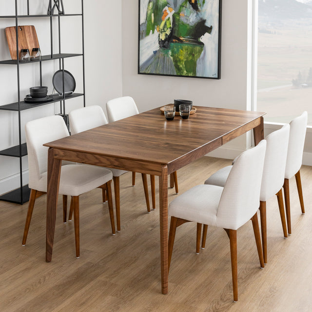 Table a manger en bois noyer avec pieds effiles et chaises blanches sur parquet clair.