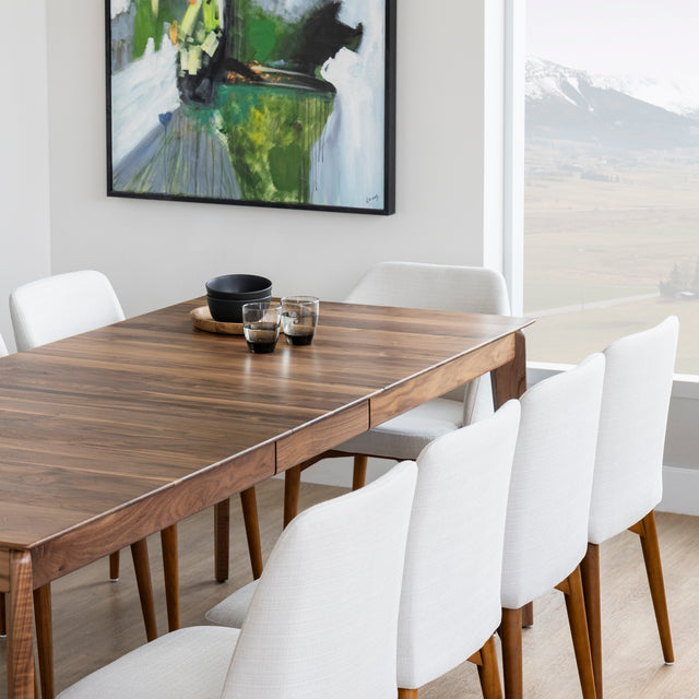 Table a manger en bois noyer avec pieds effiles et chaises blanches sur parquet clair.