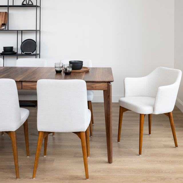 Table a manger en bois noyer avec pieds effiles et chaises blanches sur parquet clair.