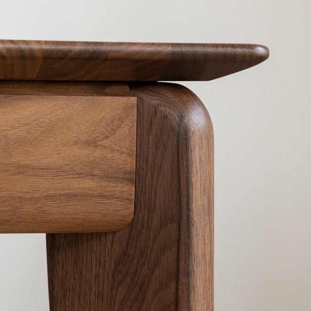 Coin de table en bois noyer avec finition lisse et bords arrondis sur parquet clair.