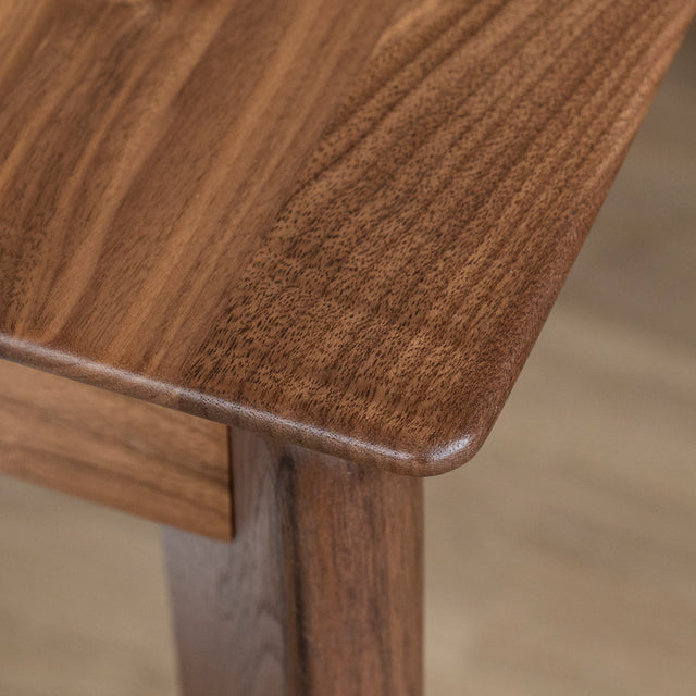 Coin de table en bois noyer avec finition lisse et bords arrondis sur parquet clair.