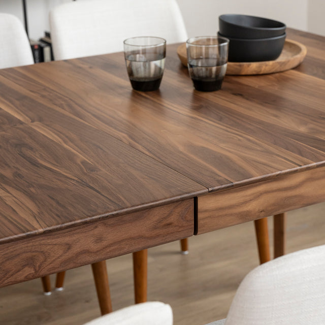 Surface de table en bois noyer avec rallonge centrale et vaisselle moderne en decoration.