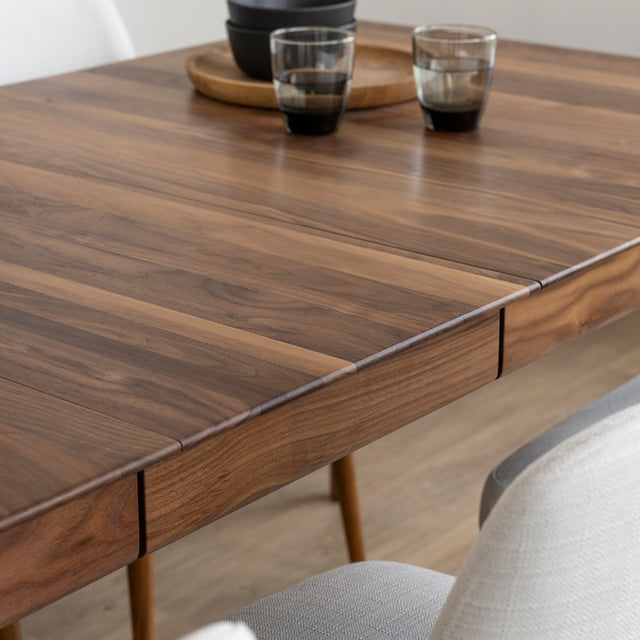 Surface de table en bois noyer avec rallonge centrale et vaisselle moderne en decoration.