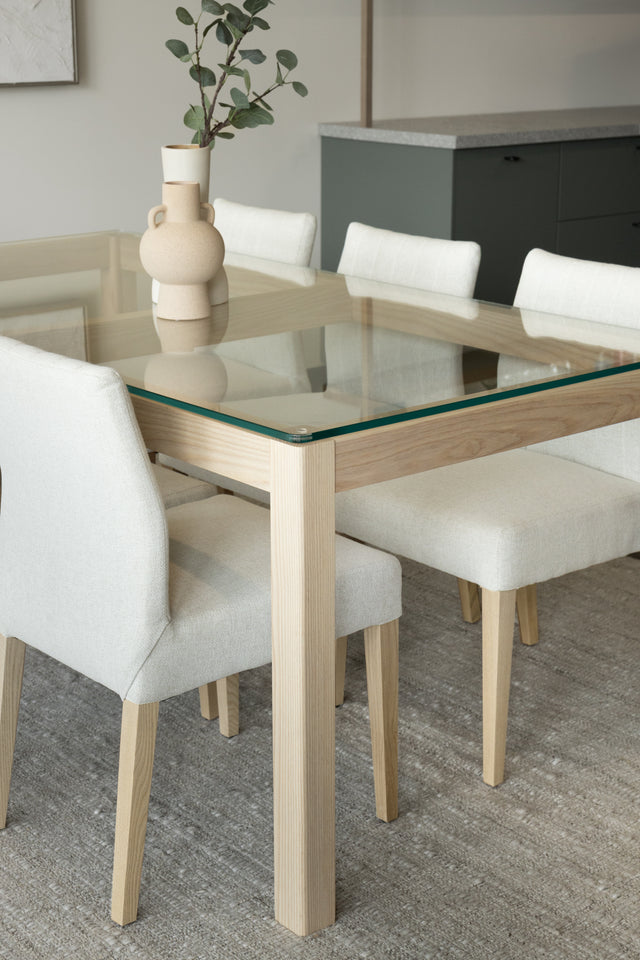 Table en verre et bois clair avec vases decoratifs et chaises beige modernes.