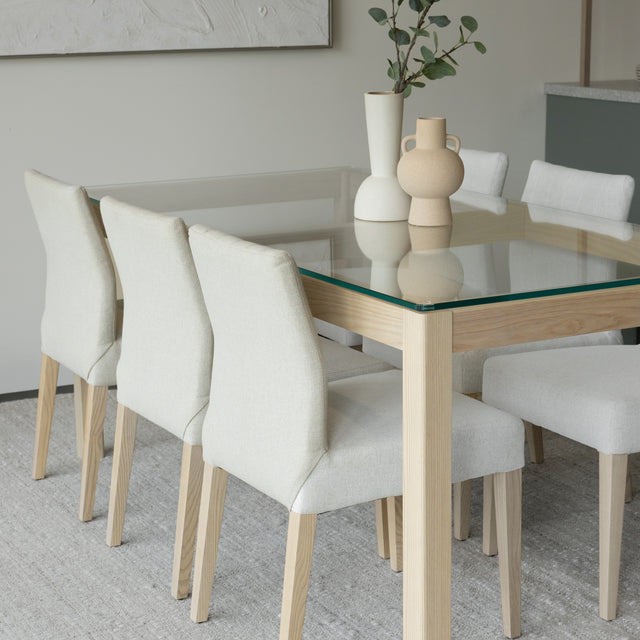 Table en verre et bois clair avec vases decoratifs et chaises beige modernes.