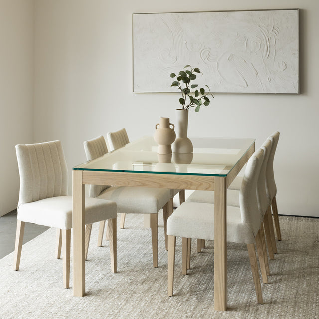 Salle a manger elegante avec table en verre et bois clair et chaises beige modernes.