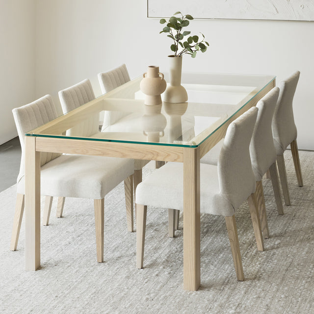 Salle a manger elegante avec table en verre et bois clair et chaises beige modernes.
