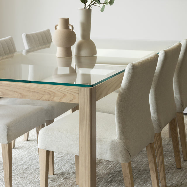 Salle a manger elegante avec table en verre et bois clair et chaises beige modernes.