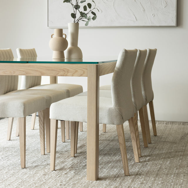Salle a manger elegante avec table en verre et bois clair et chaises beige modernes.