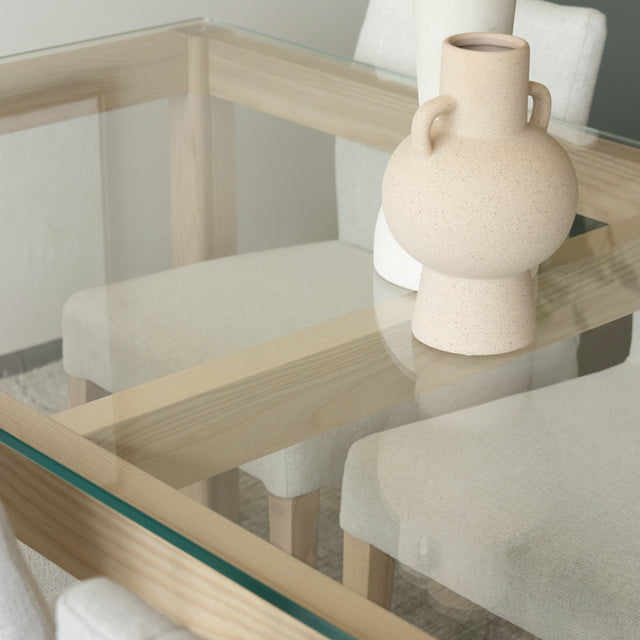 Table en verre et bois clair avec vases decoratifs et chaises beige modernes.