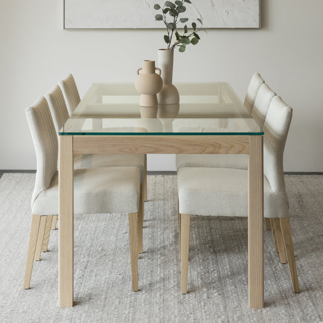 Salle a manger elegante avec table en verre et bois clair et chaises beige modernes.
