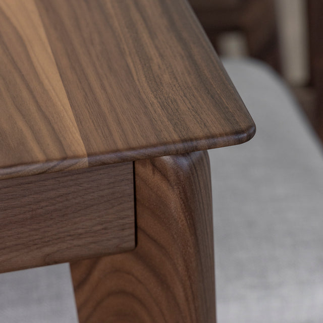 Detail du coin de table en bois noyer avec finition lisse et bords arrondis elegants.