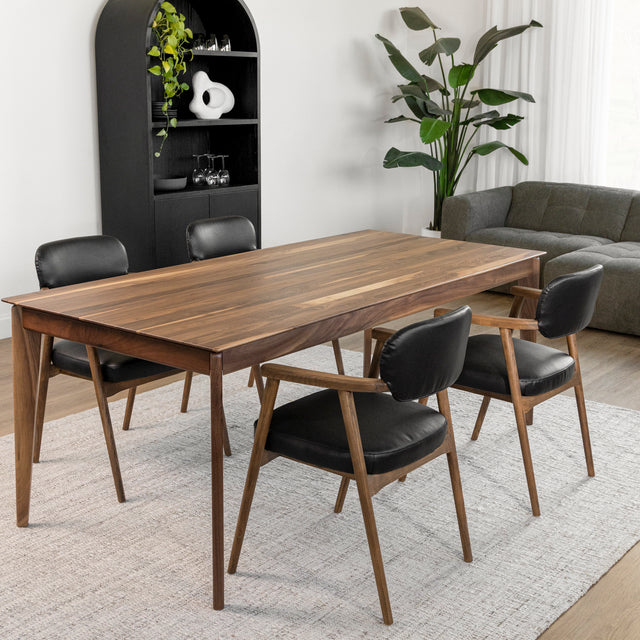 Table a manger en bois noyer avec quatre chaises noires sur tapis clair dans salle moderne.