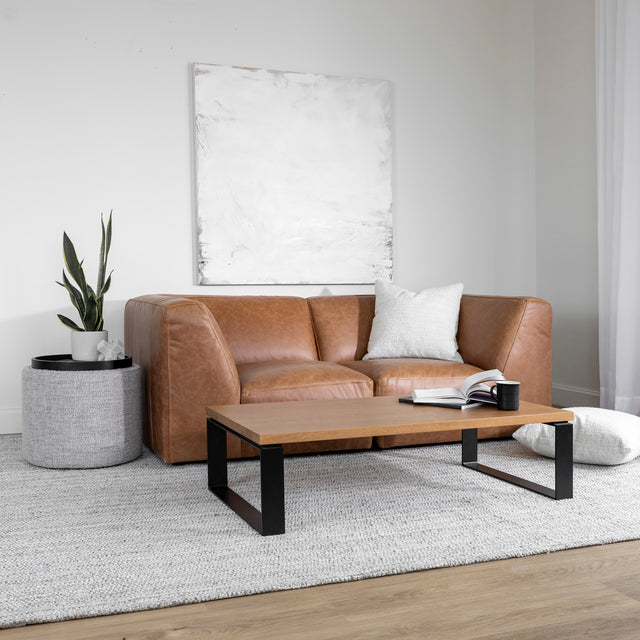 Salon moderne avec canape en cuir marron et table basse en bois clair sur tapis gris.