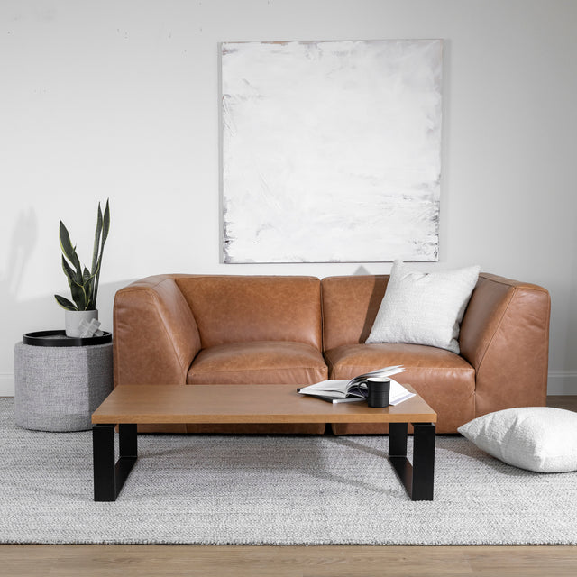 Salon moderne avec canape en cuir marron et table basse en bois clair sur tapis gris.