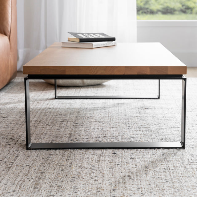 Table basse rectangulaire en bois clair avec structure en metal noir sur tapis beige.