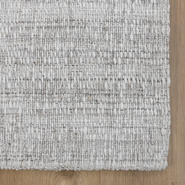 tapis tisse gris clair a texture bouclee sur parquet en bois naturel.