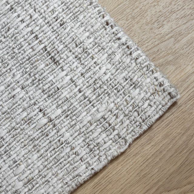 tapis tisse gris clair a texture bouclee sur parquet en bois naturel.