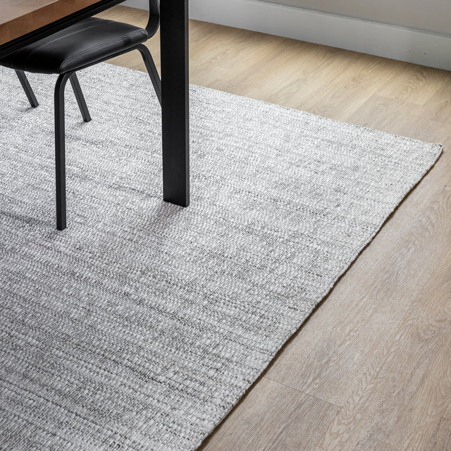 tapis gris clair a texture tissée placé sous une table a pieds noirs sur parquet en bois clair.