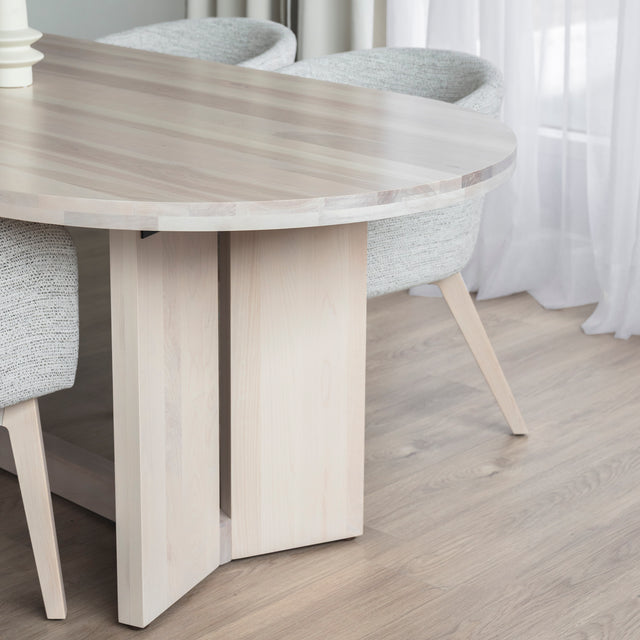 Table ovale en bois clair avec chaises crème modernes dans salle a manger lumineuse.