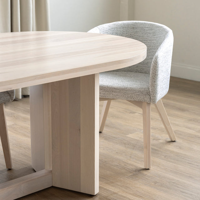 Table ovale en bois clair avec chaises crème modernes dans salle a manger lumineuse.